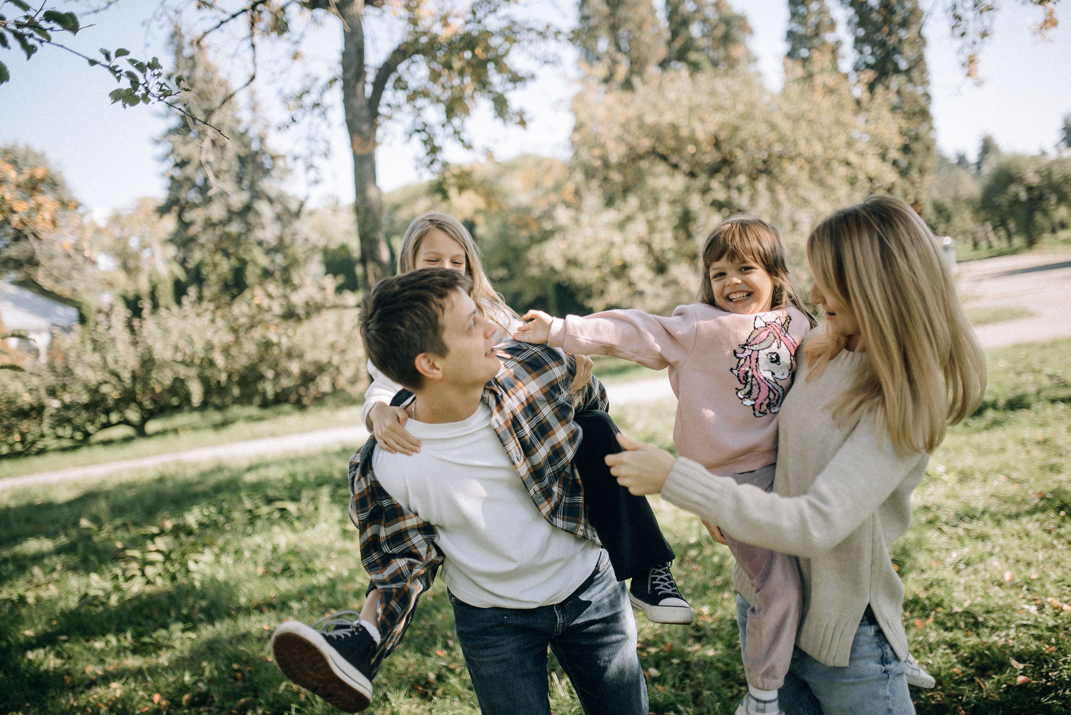 Parents carrying their two children outdoors in a park.